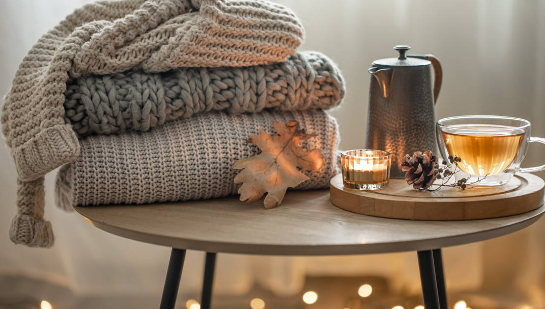 Artisans et producteurs recherchés pour le marché de Noël à la Place Montel Home autumn composition with tea and knitted sweaters in the interior of the room, on a blurred background with a garland.
